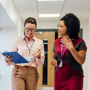 Two female teachers are walking and talking together down the school hall.